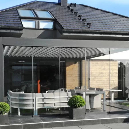 Pergola bioclimatique DETENTE à adossée lames perpendiculaires et sa façade vitrée coulissante fermée