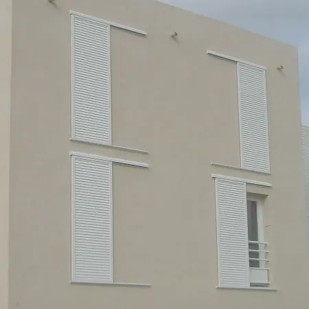 Façade d’immeuble moderne sur pilotis avec volets coulissants blancs en aluminium, installation extérieure pour fenêtres