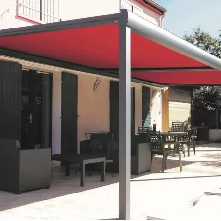 Store banne rouge déployé au-dessus d’une terrasse de maison, protection solaire extérieure avec structure aluminium.