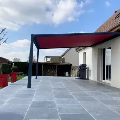 Store banne rouge déployé au-dessus d’une terrasse de maison, protection solaire extérieure avec structure aluminium. 2