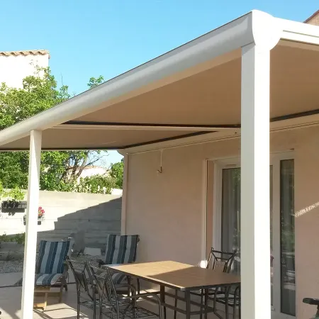 Pergola en aluminium avec toile fixe, installée sur une terrasse de maison pour créer un espace repas ombragé.
