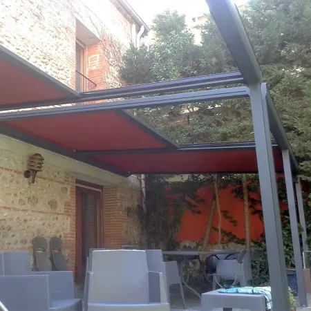 Pergola en aluminium avec toile rétractable rouge, installée sur une terrasse de maison en pierre pour créer une zone ombragée.
