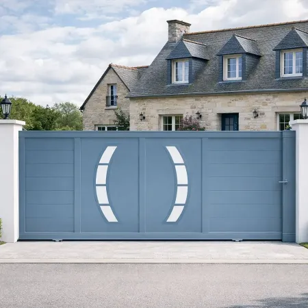 Portail coulissant en aluminium RAL 5014 intégré dans une clôture avec piliers blancs devant une maison bretonne en pierre