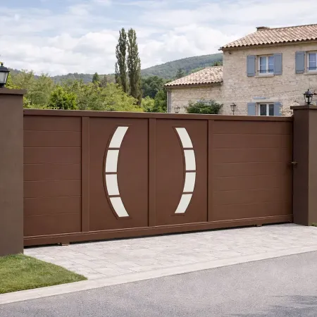 Portail coulissant en aluminium RAL 8014 vu de côté, intégré dans une clôture avec haies et piliers devant une maison provençale