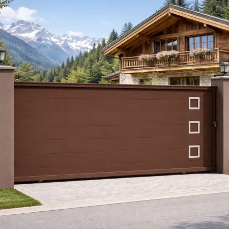Portail coulissant en aluminium RAL 8014 vu de côté, intégré dans une clôture avec haies et piliers devant un chalet de montagne
