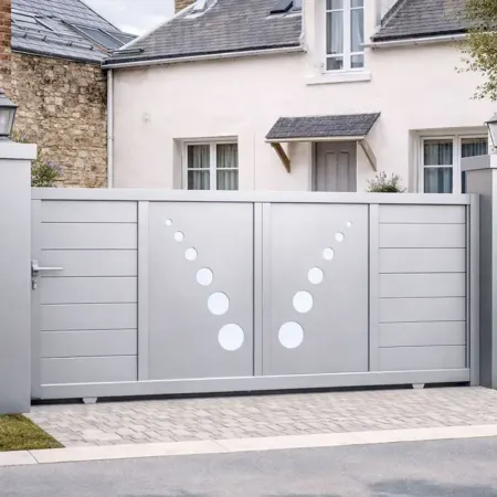 Portail coulissant en aluminium RAL 9006 avec motifs circulaires, intégré dans une clôture en pierre, devant une maison de ville