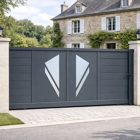 Portail coulissant en aluminium RAL 7016 vu de côté, intégré dans une clôture avec piliers en pierre devant une maison ancienne