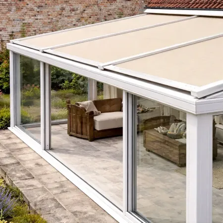 Vue de côté d’un store de toiture pour véranda avec toile beige, installé sur une véranda en aluminium adossée à une maison