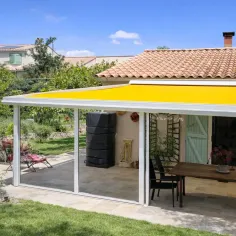 Vue de côté d’un store de toiture pour véranda avec toile beige, installé sur une véranda en aluminium adossée à une maison 2