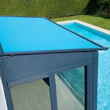 Store de toiture pour véranda avec toile bleu lagon, structure en aluminium anthracite, installé à proximité d’une piscine