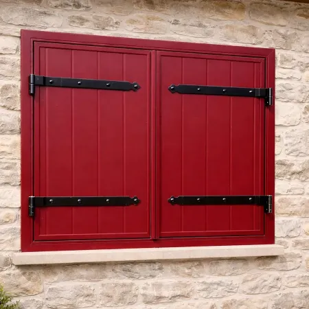 Volet battant aluminium RAL 3005 rouge bordeaux avec précadre assorti, installé sur façade en pierre naturelle.