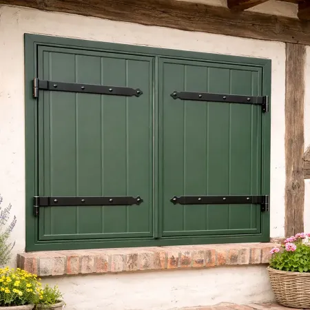 Volet battant aluminium vert avec ferrures noires installé sur façade à colombages de maison rustique, avec décoration florale.