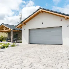 Porte de garage sectionnelle gris clair sur maison moderne avec allée pavée et architecture contemporaine extérieure
