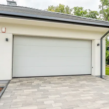 Porte de garage sectionnelle blanche installée sur maison moderne avec allée pavée et extérieur résidentiel contemporain