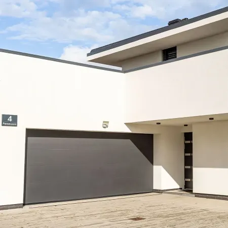 Porte de garage sectionnelle gris anthracite installée sur maison contemporaine avec façade moderne et allée pavée extérieure