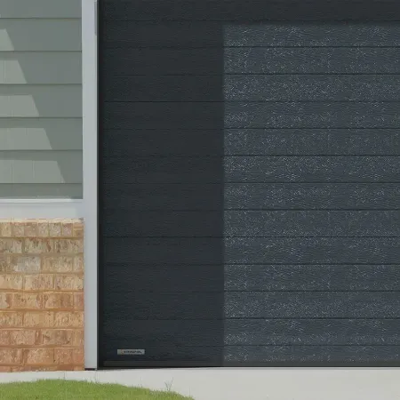 Détail porte de garage sectionnelle noire avec texture effet bois installée sur façade de maison en brique style américain