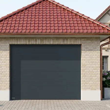 Porte de garage sectionnelle anthracite installée sur maison en brique avec toiture en tuiles rouges et extérieur paysager