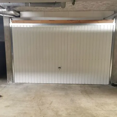 Porte de garage basculante blanche installée dans un box en sous-sol, avec structure béton et système de fermeture central