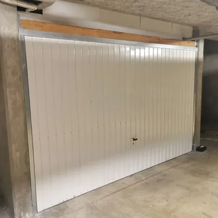 Porte de garage basculante blanche dans un box, structure métallique et système de fermeture central