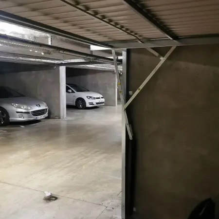Porte de garage basculante ouverte dans un parking en sous-sol avec structure métallique et véhicules stationnés