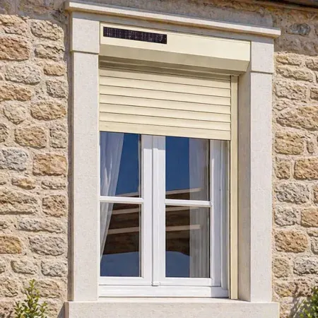 Volet roulant solaire RAL 1015 installé sur fenêtre de maison en pierre avec encadrement moderne et façade extérieure