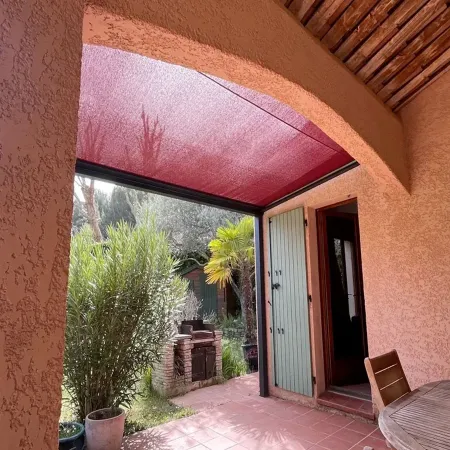 Pergola aluminium à toile enroulable rouge sur mesure installée sur terrasse avec jardin méditerranéen