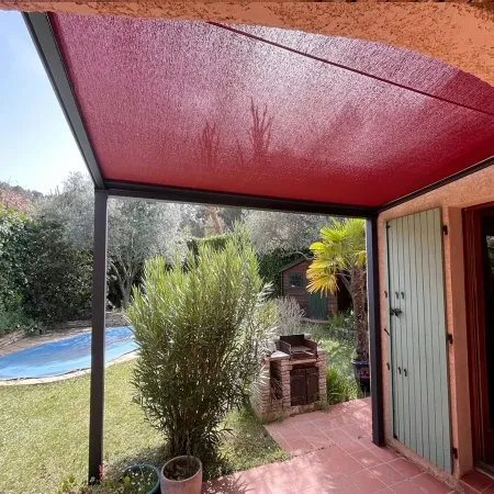 Pergola aluminium à toile enroulable rouge sur mesure couvrant une terrasse avec piscine, barbecue et jardin méditerranéen