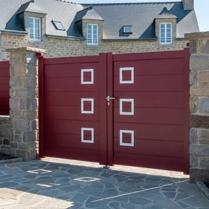 Portail aluminium CLAVER bordeaux devant une maison en pierre de taille