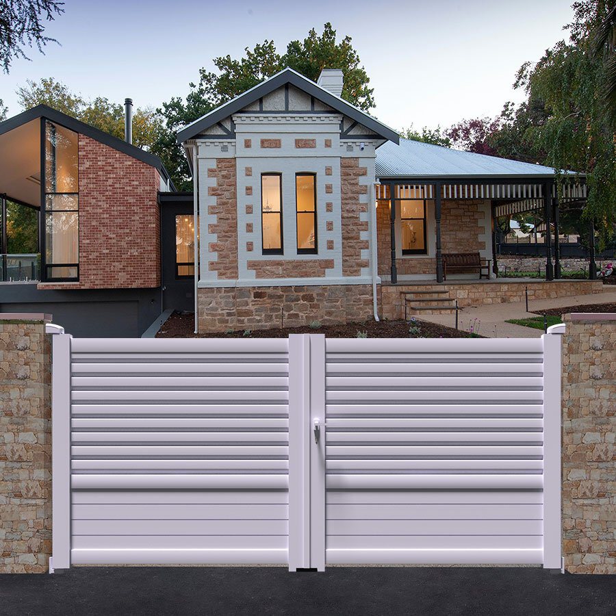 Portail aluminium DAD blanc entre deux piliers, devant une maison ancienne