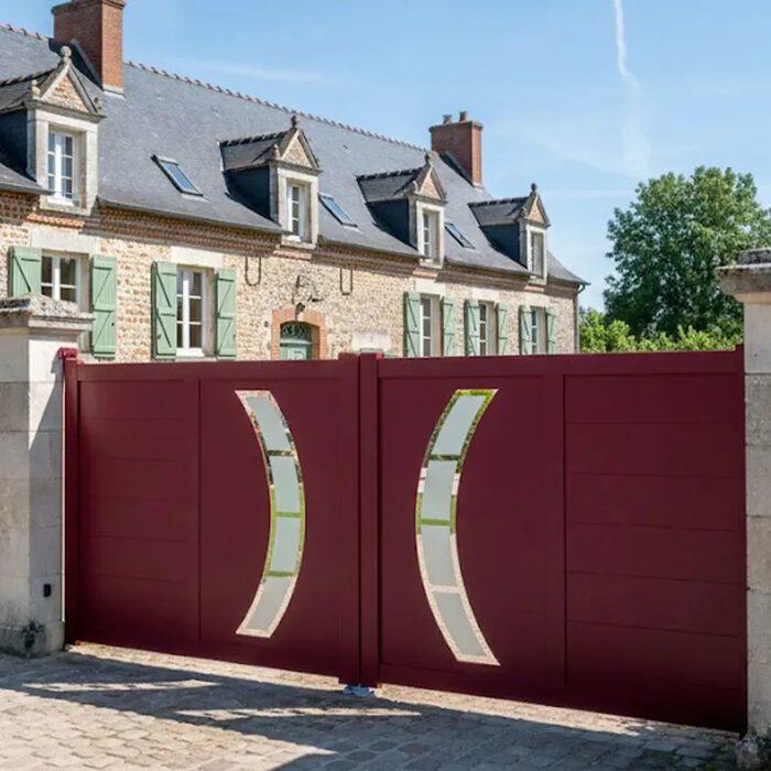 Portail aluminium DALL rouge devant une maison en pierre