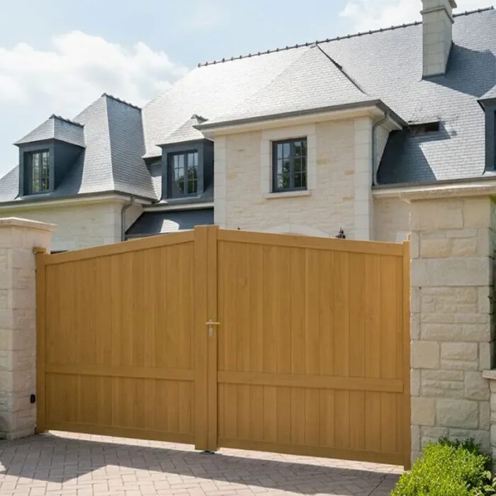Portail aluminium SEA chêne doré devant une maison en pierre de taille