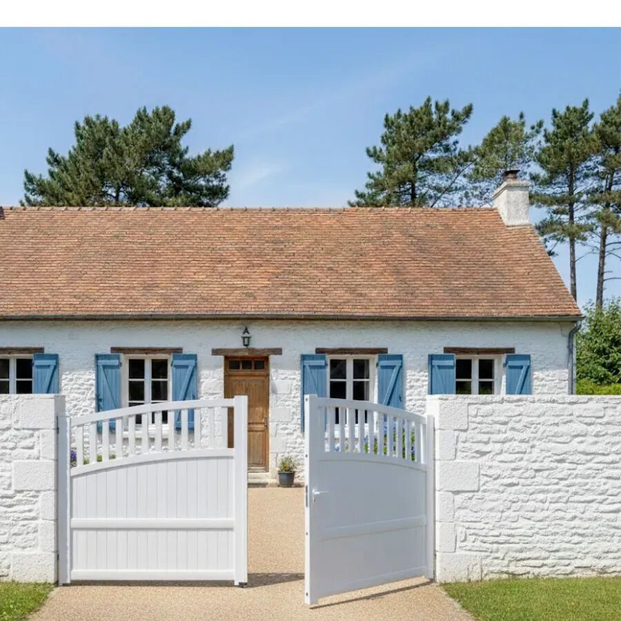 Portail aluminium TOM blanc entre deux piliers, devant une maison bretonne