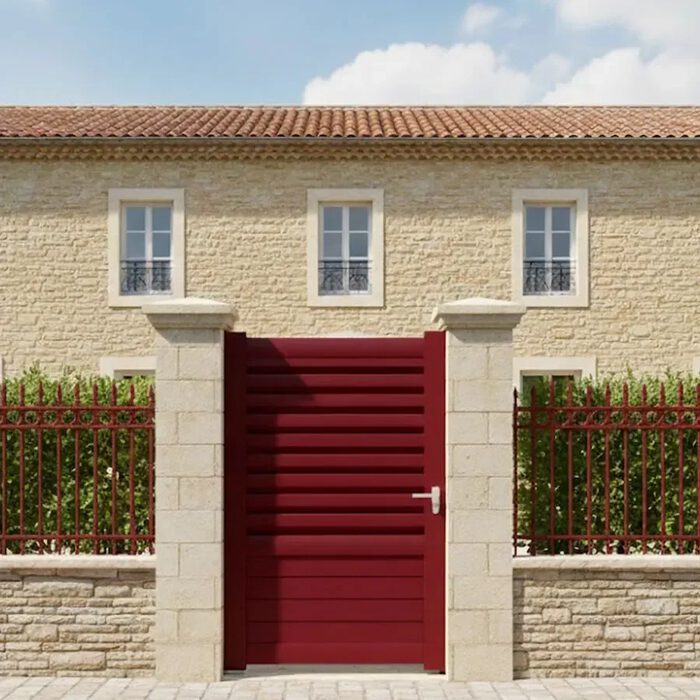 Portillon aluminium DAD rouge devant une maison en pierre