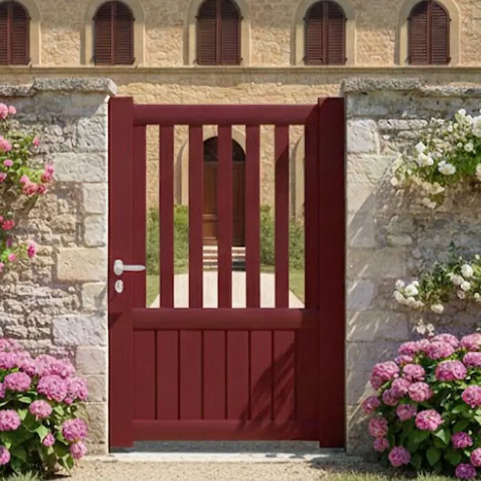 Portillon aluminium KIN rouge devant une maison en pierre