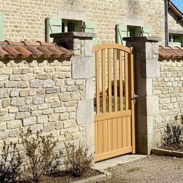 Portillon aluminium PIL chêne doré devant un mur en pierre