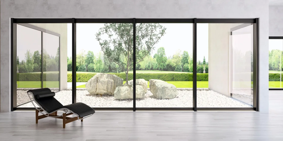 Grande baie coulissante aluminium 4 vantaux noire vue de l'intérieur, ouverte sur un jardin minéral
