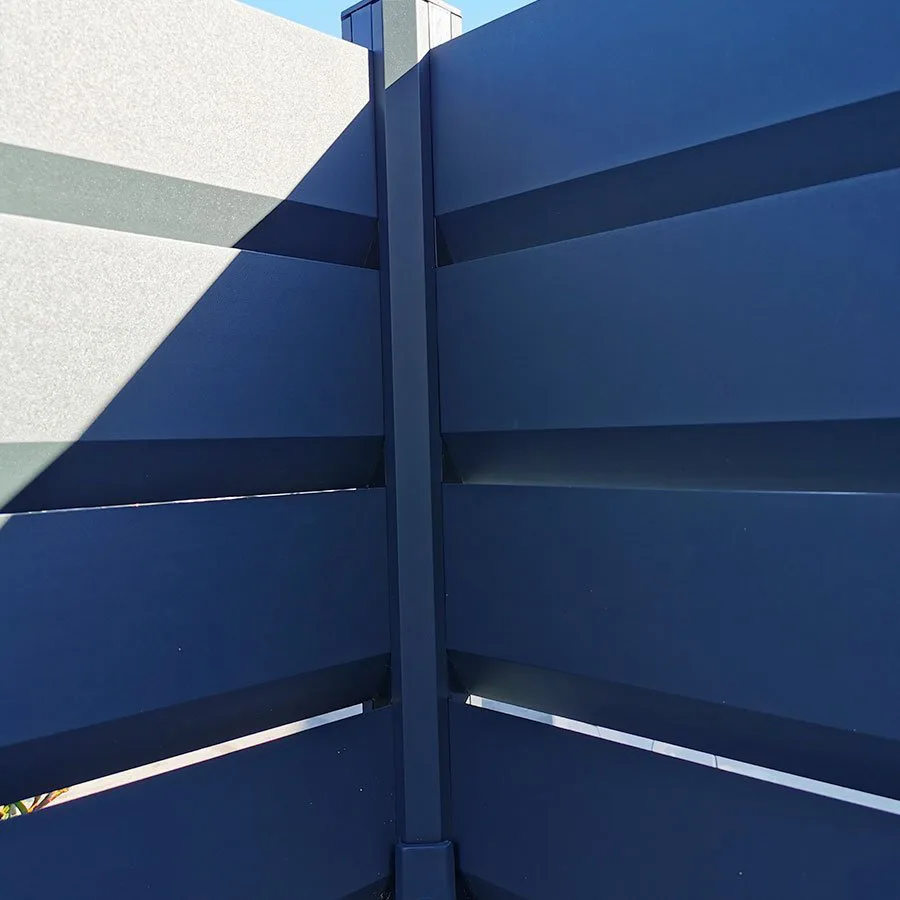 Gros plan d'une clôture brise vue aluminium bleu nuit : poteau, lames à recouvrement et ombres portées