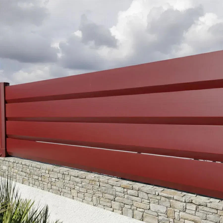 Clôture brise vue aluminium rouge RAL 3005 sur un muret en pavés, ciel nuageux