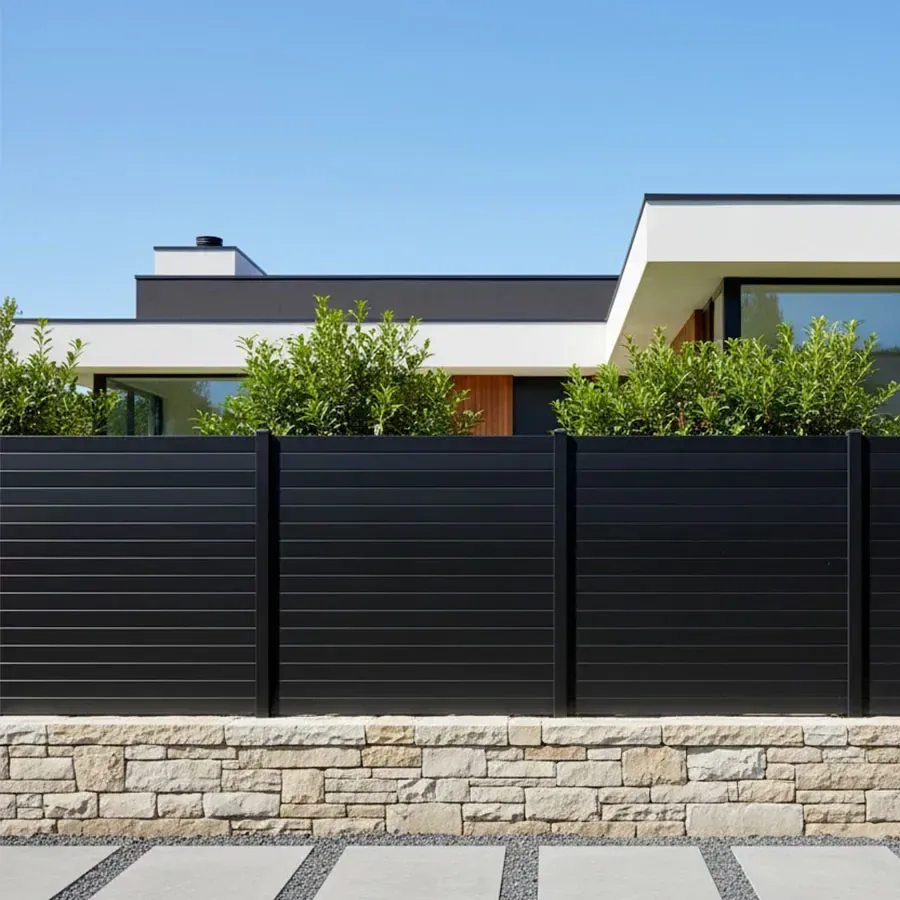 Clôture aluminium noire à petites lames pleines de 100 mm sur un muret en pierre devant une maison contemporaine