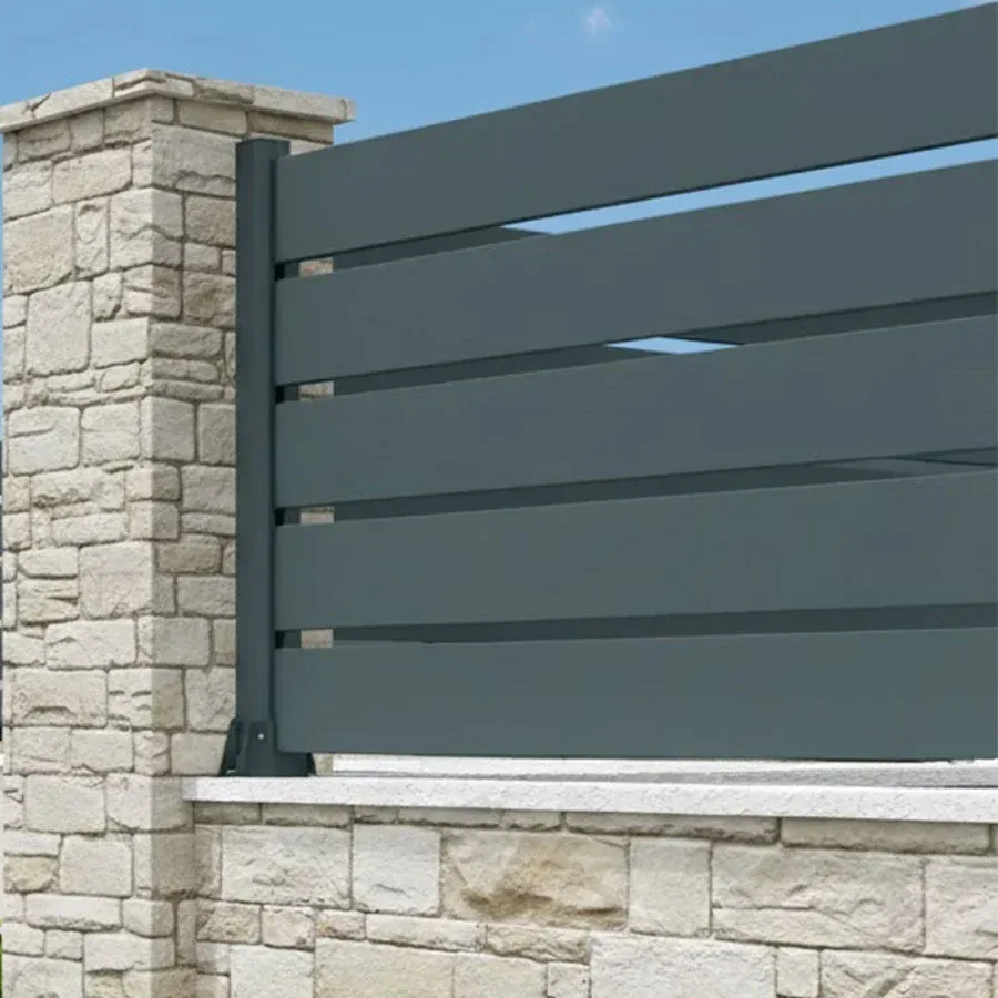 Gros plan d'une clôture aluminium anthracite à grandes lames ajourées contre un pilier en pierre