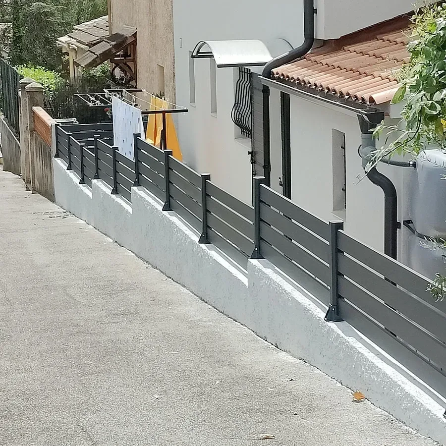 Clôture aluminium anthracite à petites lames ajourées posée en redans le long d'une allée en pente