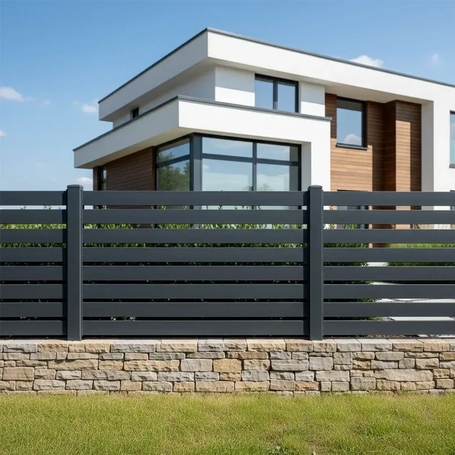 Clôture aluminium anthracite RAL 7016 à petites lames ajourées sur un muret en pierre devant une maison contemporaine