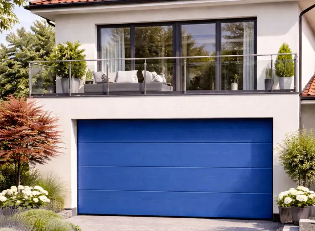 Porte sectionnelle de garage bleu gentiane mat RAL 5010 sous maison à étage avec façade claire et toiture en tuiles