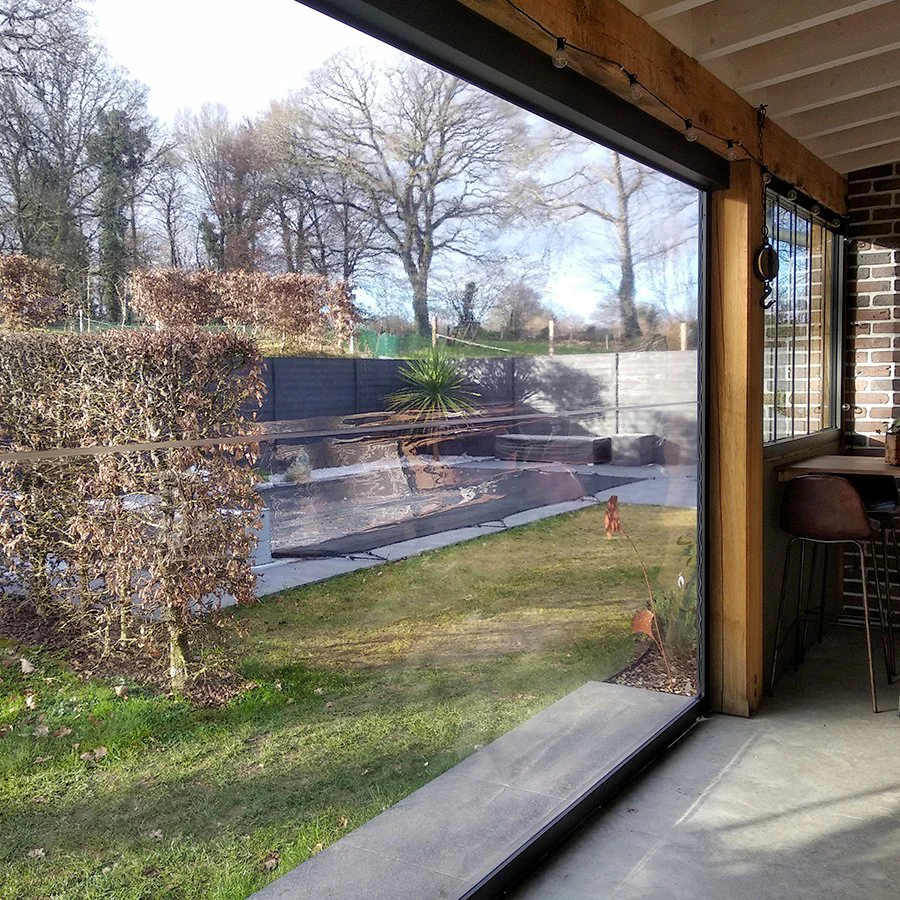 Store vertical à toile Cristal transparente fermant une terrasse couverte, le jardin reste entièrement visible