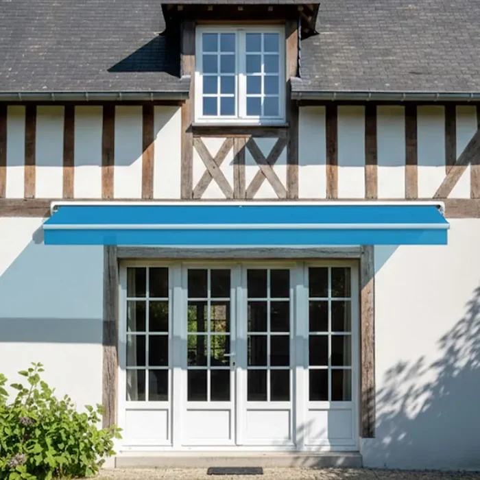 Store banne à coffre bleu replié au-dessus d'une porte-fenêtre de maison à colombages