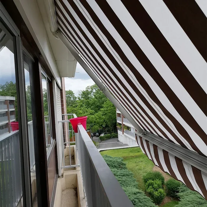 Store banne traditionnel à toile rayée manœuvré au treuil et à la manivelle depuis un balcon