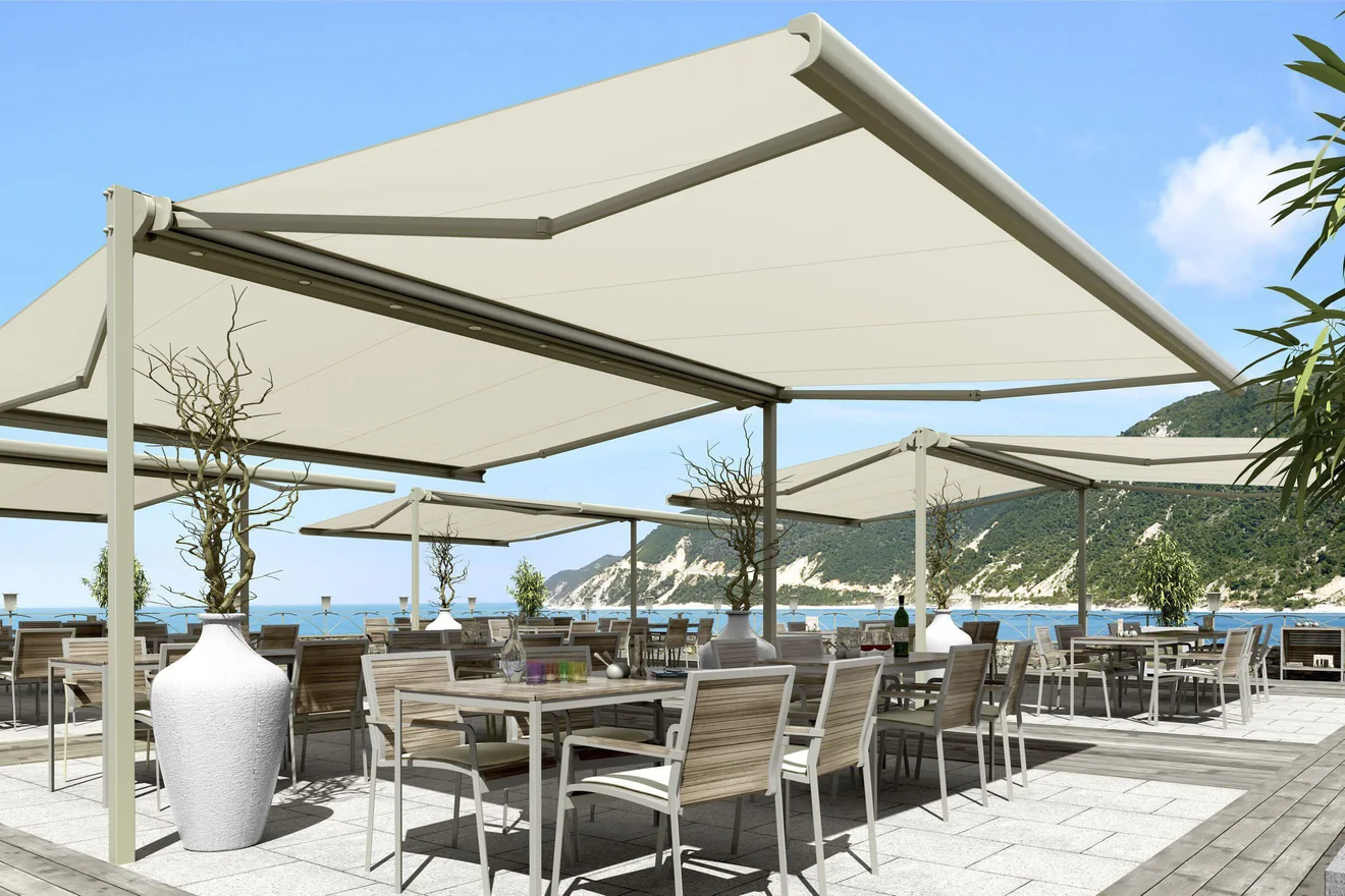Stores terrasse double pentes XL écru sur une terrasse de restaurant en bord de mer, coffre central et pieds visibles