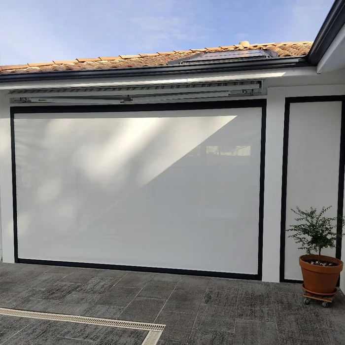 Store vertical enroulant gris devant une grande baie vitrée de maison en pierre