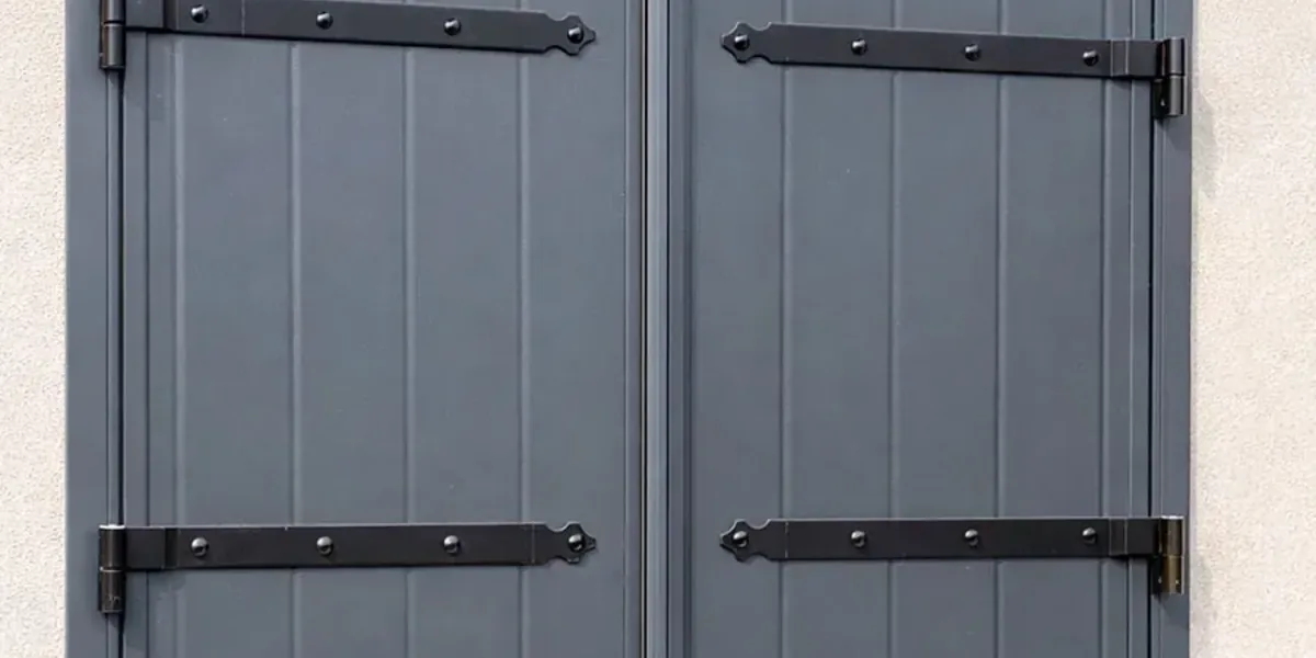 Volet battant aluminium gris anthracite à deux vantaux avec précadre, sur une façade en enduit clair