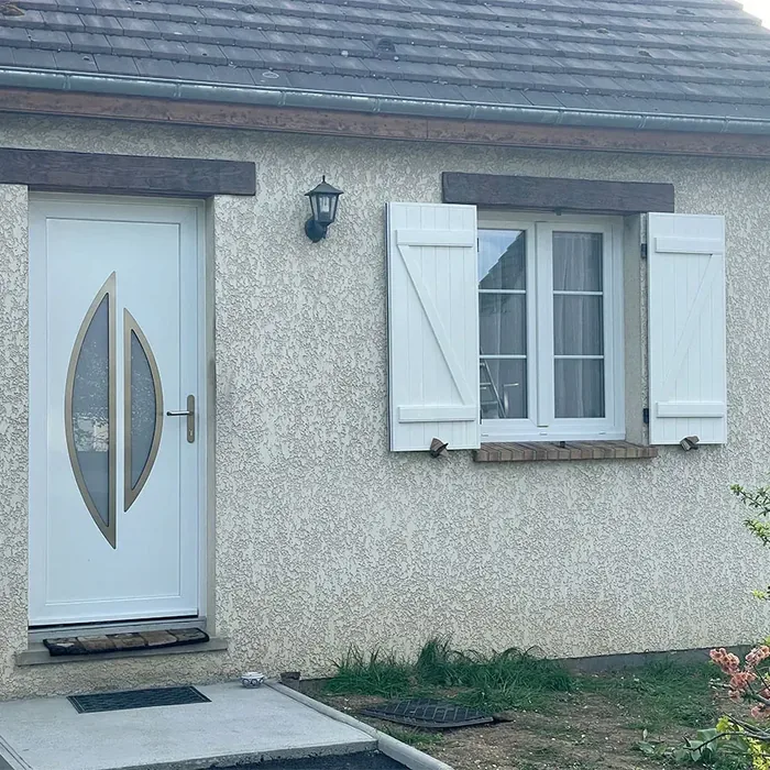 Volets battants aluminium blancs sur une fenĂȘtre traditionnelle et une porte d'entrĂ©e vitrĂ©e, façade en enduit grattĂ©